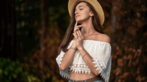 Frau im Boho-Chic Style mit Hut und luftigem Oberteil im Wald, verträumte Pose