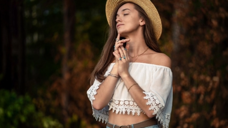 Frau im Boho-Chic Style mit Hut und luftigem Oberteil im Wald, verträumte Pose