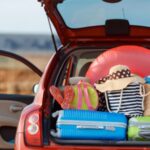 Rotes Auto von hinten mit offenem Kofferraum,in welchem große Menge an Gepäck gelagert wird