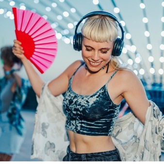 Frau mit Glitzer-Top, Kopfhörern auf dem Kopf und pinkem Fächer in der Hand auf einem Festival
