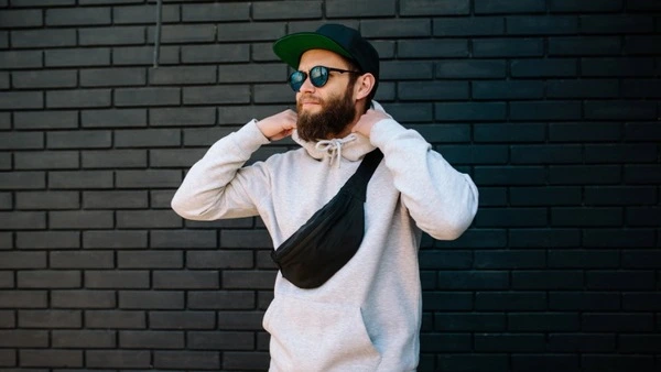 Festivalbesucher mit weißem Hoodie, Sonnenbrille, Cap und Crossbody-Tasche – lässiger Streetwear-Look für Herren auf dem Festivalgelände.
