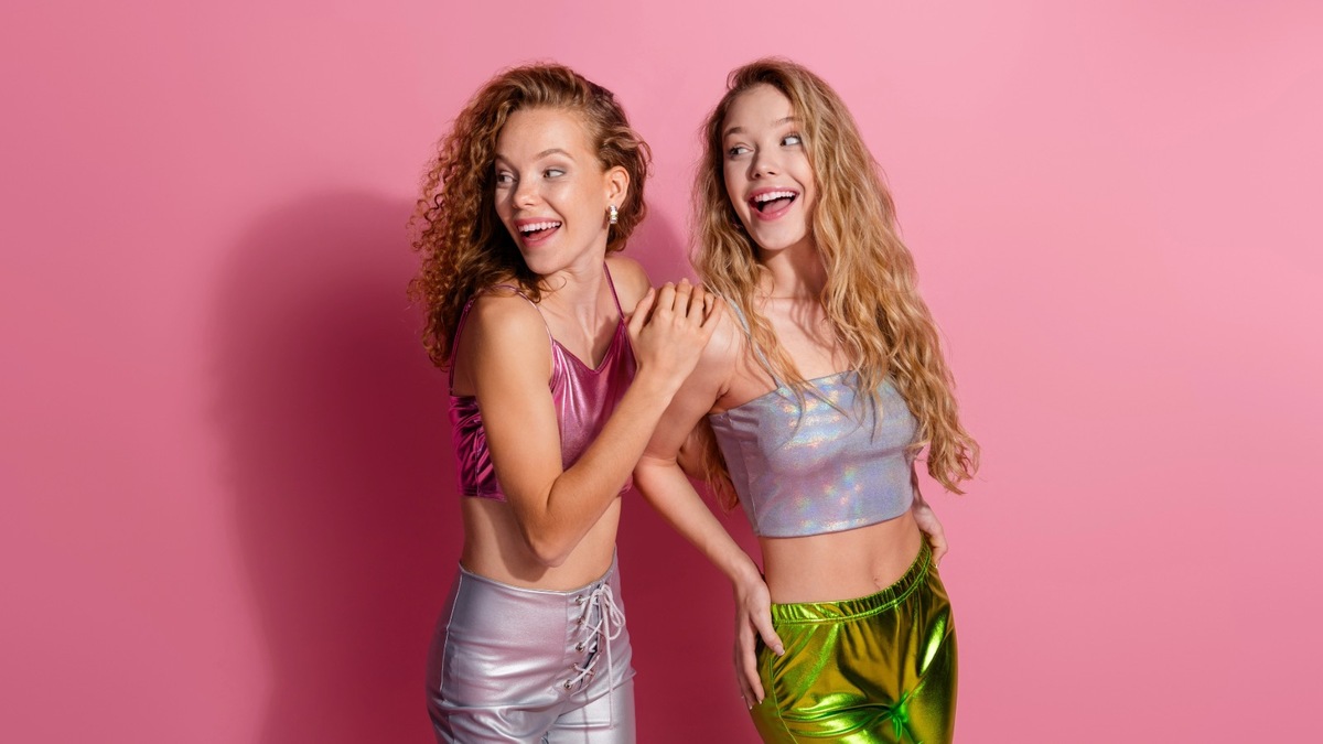 Zwei Frauen in funkelnder Glitzerkleidung vor rosa Hintergrund