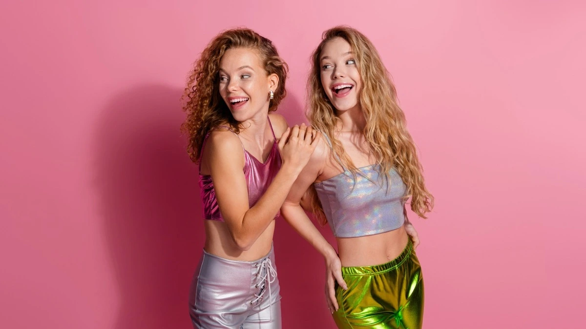 Zwei Frauen in funkelnder Glitzerkleidung vor rosa Hintergrund